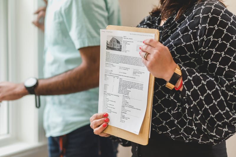 An agent holding a printed MLS listing sheet on a clipboard