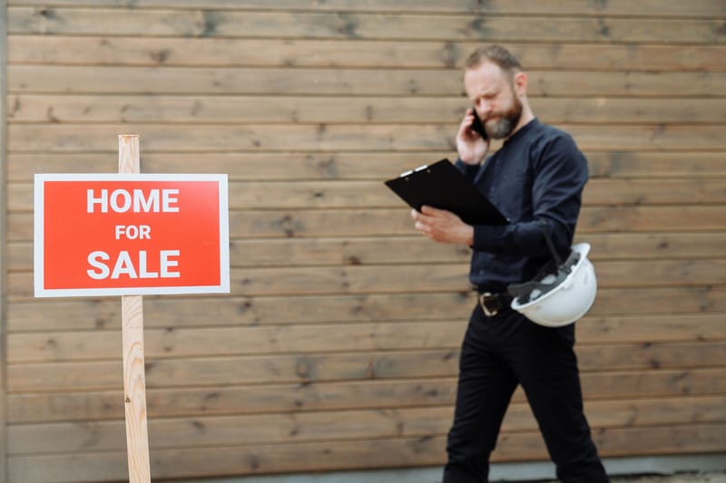 An agent on a call outside a home for sale, clipboard in hand