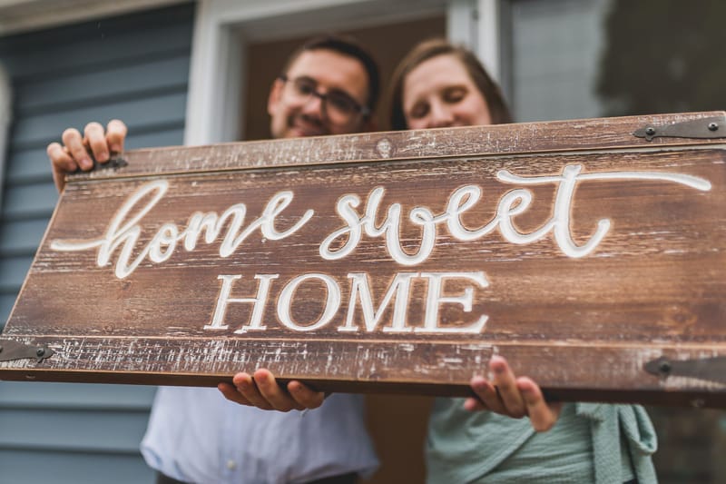 New homeowners on their porch with a home-sweet-home sign